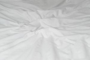 White crumpled or wrinkled bedding sheet or blanket with pattern after guest's use taken in hotel, resort room with copy space, Untidy blanket background texture photo