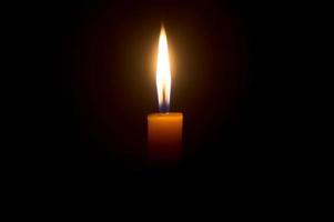 una sola llama de vela encendida o una luz que brilla en una vela amarilla aislada en un fondo negro u oscuro en la mesa de la iglesia para Navidad, funeral o servicio conmemorativo