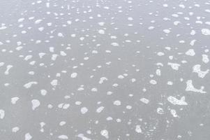 blurred photo of gray or dark sand beach surface with small foams spreading on top