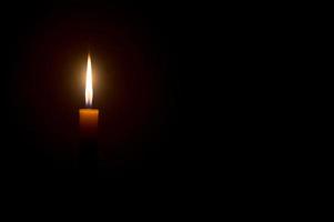 A single burning candle flame or light glowing on a Single small yellow candle light glowing is isolated on black or dark background on table in church or temple for Christmas, funeral or memorial photo