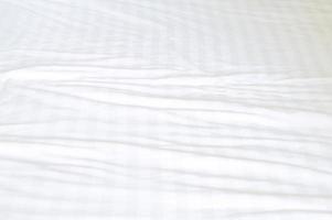 White wrinkled bedding sheet with pattern after guest's use was taken in hotel room with copy space, Untidy blanket background texture photo
