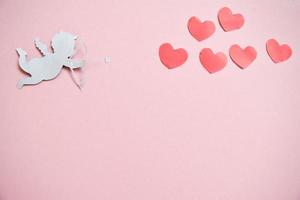 concepto del día de san valentín. corazones de color rojo y cupido apuntando en el corazón sobre fondo rosa. tarjetas del día de san valentín. foto