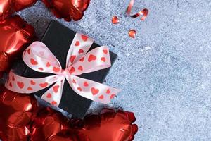 globos con forma de corazón rojo y caja de regalo sobre fondo de hormigón. plantilla de tarjeta de felicitación del día de san valentín. copie el espacio foto