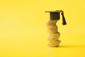 Graduated cap with coins on yellow background. Savings for education concept. Copy space photo