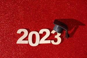 concepto de clase de 2023. números 2023 con gorra negra graduada sobre fondo rojo brillante foto