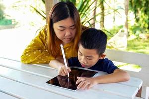 Mother teaches son to use tablet to learn online. Concept adult teaching children, family relations, family, learning outside the classroom, outside activities.soft and selective focus. photo