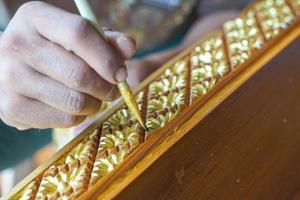 painter using paintbrush Paint gold on Thai carved patterns to decorate wooden furniture before being sold. Soft and selective focus. photo