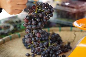 The customer picks up a bunch of seedless grapes in a bamboo basket to buy from gardeners. soft and selective focus. photo