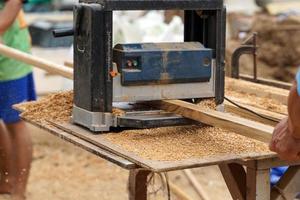 A carpenter is using a thickness planer to roll a sheet of wood to have a consistent thickness to be suitable for woodworking. Soft and selective focus. photo