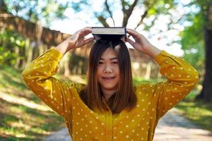 mujer asiática con un libro en la cabeza mientras lee un libro en el parque. enfoque suave y selectivo foto