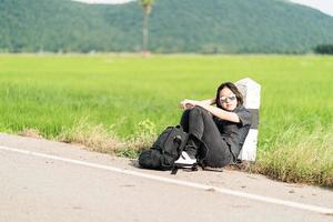 Woman sit with backpack hitchhiking along a road photo