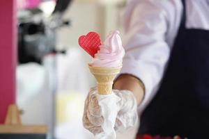 A worker with gloves holding an ice cream cone with a mix flavours pink and vanilla. Pink ice cream with a red heart. photo