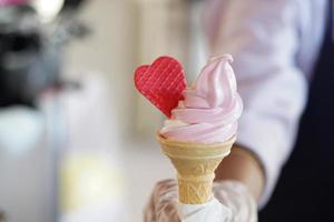 A worker with gloves holding an ice cream cone with a mix flavours pink and vanilla. Pink ice cream with a red heart. photo