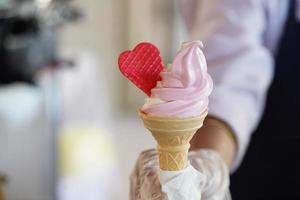 A worker with gloves holding an ice cream cone with a mix flavours pink and vanilla. pink ice cream with a red heart. photo