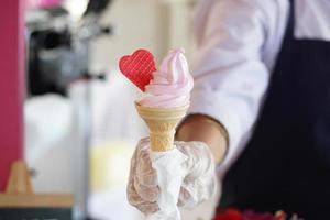 A worker with gloves holding an ice cream cone with a mix flavours pink and vanilla. pink ice cream with a red heart. photo