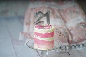 21st Birthday cake pink and silver cake with some sprinkles and 21st candlelight with a woman dress at the background. photo