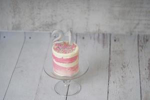 21st Birthday cake pink and silver cake with some sprinkles and 21st candlelight on a white wooden background. photo