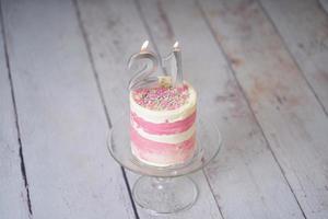 21st Birthday cake pink and silver cake with some sprinkles and 21st candlelight on a white wooden background. photo