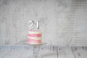 21st Birthday cake pink and silver cake with some sprinkles and 21st candlelight on a white wooden background. photo