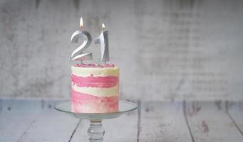 21st Birthday cake pink and silver cake with some sprinkles and 21st candlelight on a white wooden background. photo