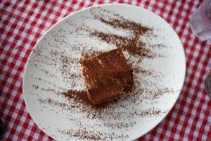 Tiramisu cake with chocolate powder decoration on a plate. Fancy red checks pattern background. Top view. photo