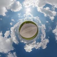 tiny planet in blue overcast sky with beautiful clouds with transformation of spherical panorama 360 degrees. Spherical abstract aerial view. Curvature of space. photo