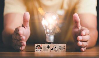 Light bulbs placed on wooden blocks and human hands on table ,target ideas and business strategies,through planning and teamwork To analyze and develop company performance from growth data to future photo