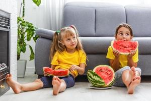 Child eating watermelon, two little girls eat watermelon at home photo