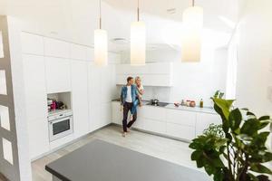 feliz pareja encantadora bebiendo vid mientras se sienta en la cocina y mira la ventana foto