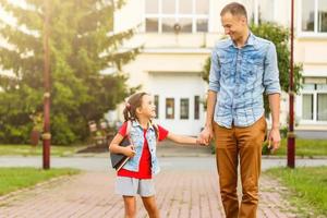 first day at school. father leads a little child school girl in first grade photo