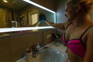 Cleanness in every move. Woman cleans mirror with help of green cloth and special mean of cleaning photo