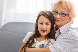 adorable niña juguetona con una niñera feliz de mediana edad en casa. linda nieta preescolar pequeña con abuela anciana emocionada. foto