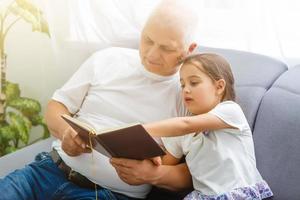 niña feliz con el abuelo leyendo un libro de cuentos en casa foto