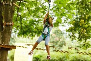 Niña de la escuela feliz disfrutando de la actividad en un parque de aventura de escalada en un día de verano foto