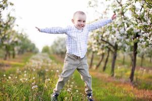 un niño feliz en un floreciente jardín primaveral juega, salta, está de buen humor. foto