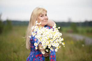 hermosa mujer de talla grande con cabello blanco en un vestido de verano posando al aire libre con margaritas. una chica regordeta en un prado le tiende la mano con un ramo de flores. foto