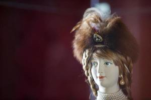 The face of an old retro porcelain doll in a fur hat on a burgundy background. photo