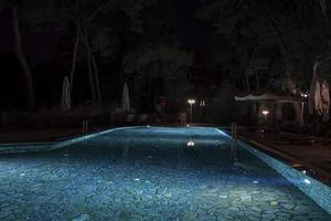 Parasols and deck chairs by illuminated swimming pool at resort photo