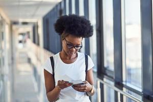 Young african american female passanger in casual clothes is in airport with tickets in hands photo