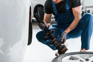 Close up view of man in work uniform that repairs white automobile indoors. Conception of automobile service photo