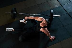 vista superior de un hombre fuerte con ropa deportiva que se sienta en el suelo y toma un descanso en el gimnasio foto