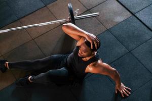 Sitting on the floor. Strong african american man in sportive clothes have workout day in the gym photo