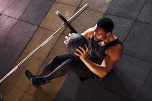 Sitting on the floor. Strong african american man in sportive clothes have workout day in the gym photo