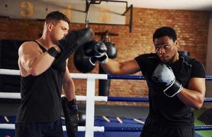 tener el boxeo practicando. un hombre afroamericano con un hombre blanco tiene un día de entrenamiento en el gimnasio foto