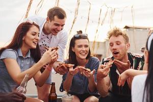 With delicious pizza. Group of young people in casual clothes have a party at rooftop together at daytime photo