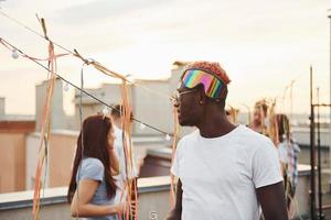 posando para una cámara. un grupo de jóvenes con ropa informal tienen una fiesta en la azotea juntos durante el día foto