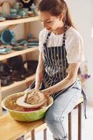 Young female ceramist working by using pottery wheel indoors and making handmade clay product photo