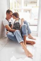 Cute young couple in jeans sitting down on the floor and embracing each other photo