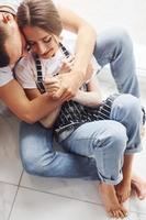 Cute young couple in jeans sitting down on the floor and embracing each other photo