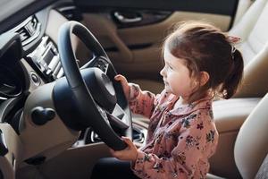 Cute little girl sitting on the driver's seat inside of modern car photo